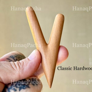 May include: A V-shaped wooden tool with a smooth, light brown finish and a pointed bottom end. The surface features a natural wood grain pattern. The text "HanaqPacha" is visible in the background, and the text "Classic Hardwood" is printed on the right.