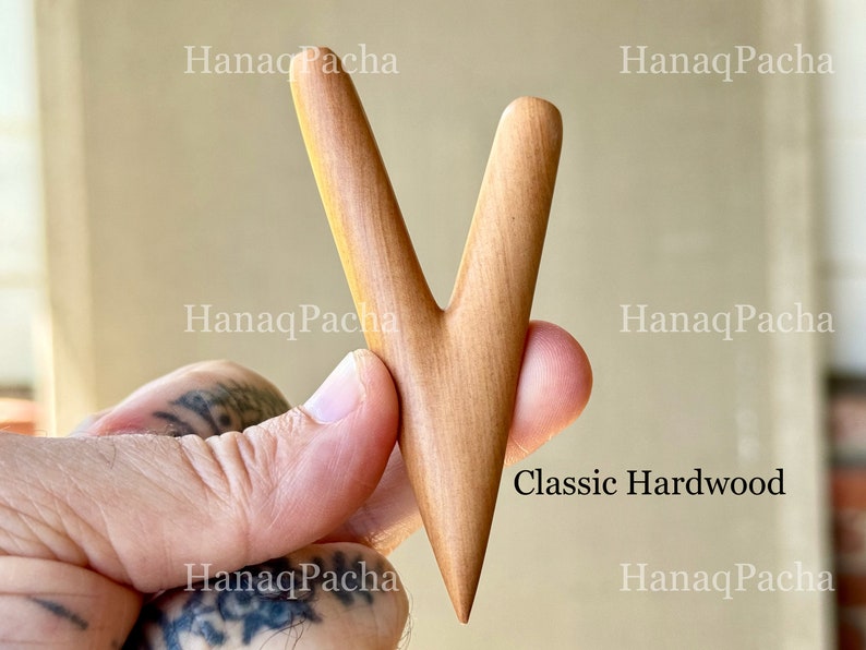 May include: A V-shaped wooden tool with a smooth, light brown finish and a pointed bottom end. The surface features a natural wood grain pattern. The text "HanaqPacha" is visible in the background, and the text "Classic Hardwood" is printed on the right.