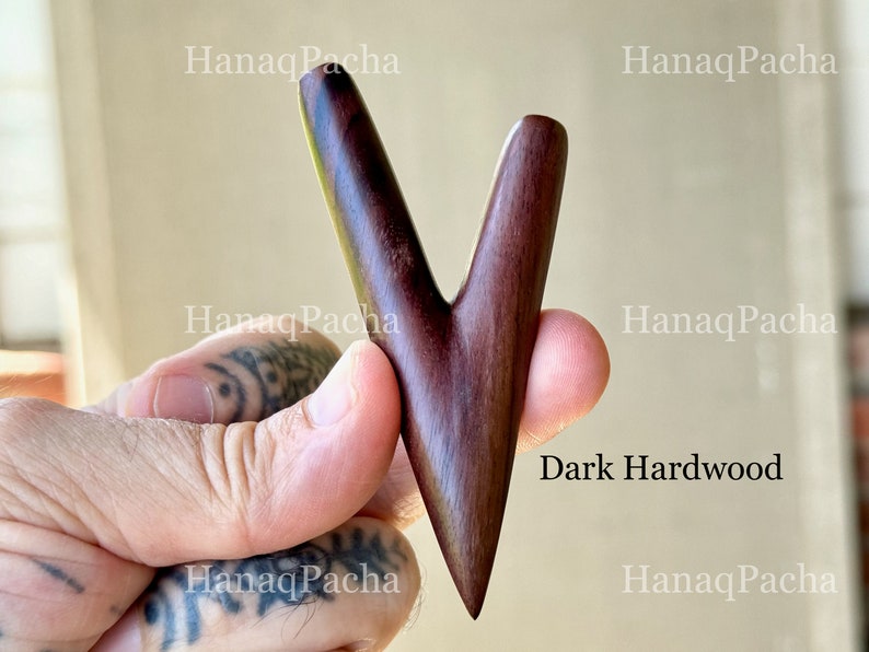 May include: A V-shaped dark hardwood tool with a smooth, polished finish and a pointed base. The object features a bifurcated top section with two rounded prongs. The text "HanaqPacha" is visible in the background, and "Dark Hardwood" is printed.