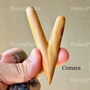 May include: A V-shaped wooden tool with a smooth, light brown finish and visible natural grain patterns. The object features two tapered prongs meeting at a single pointed base. The text "Cemara" is printed in black near the lower right side.