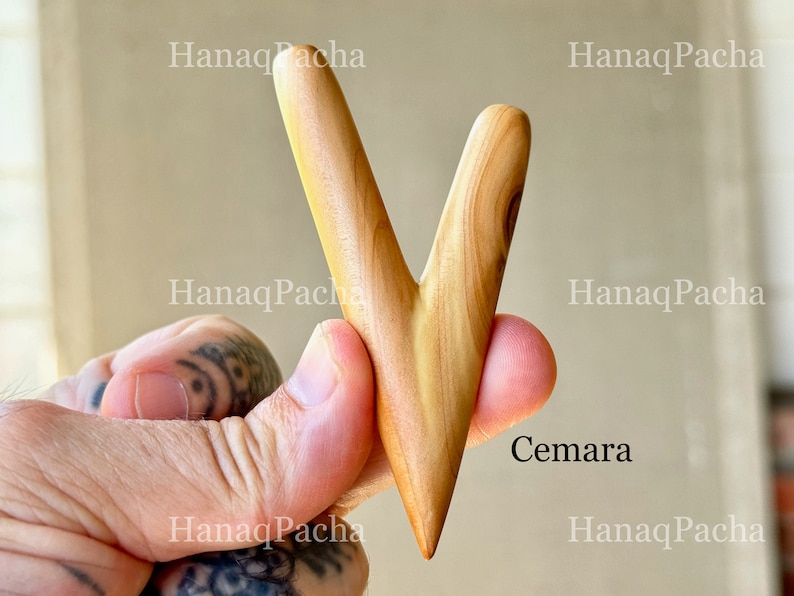 May include: A V-shaped wooden tool with a smooth, light brown finish and visible natural grain patterns. The object features two tapered prongs meeting at a single pointed base. The text "Cemara" is printed in black near the lower right side.