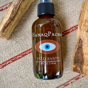 Peut inclure: Une bouteille en verre brun avec un vaporisateur noir et une &eacute;tiquette qui indique "Hanaq Pacha" et "Palo Santo All Natural Clearing Spray 4 fl. oz. (118 ml)". L'&eacute;tiquette pr&eacute;sente &eacute;galement un &oelig;il brun avec un iris bleu. La bouteille est pos&eacute;e sur un tissu ray&eacute; beige et rouge.