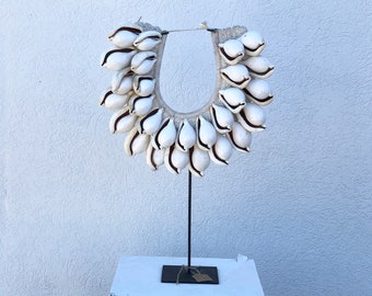 May include: A white shell necklace on a black stand. The necklace is made of many small white shells that are strung together in a circle.