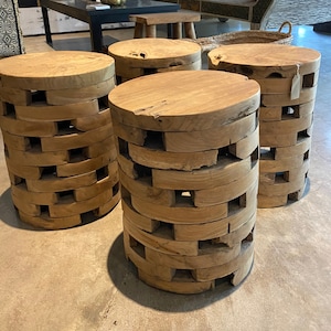 May include: Four wooden stools with a unique stacked design. Each stool is made of multiple layers of wood, creating a textured and rustic look. The stools are a natural wood color and have a circular top.