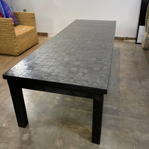 May include: A rectangular coffee table with a mosaic tile top and black legs. The tabletop is a dark gray color, and the tiles are arranged in a grid pattern. The table is approximately 60 inches long.