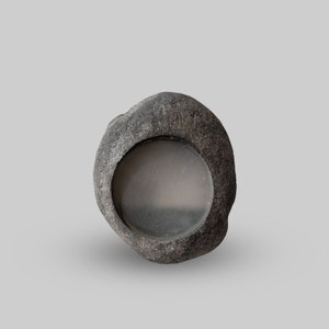 Op de afbeelding: Een grijze, steenachtige kom met een cirkelvormige inkeping. De kom heeft een ruw, getextureerd oppervlak en een glad, grijs interieur. De kom is ontworpen om kleine items in te bewaren of als decoratief stuk te dienen.