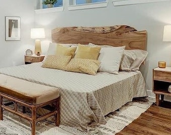 May include: A bedroom with a wooden bed frame with a live edge headboard. The bed is made with white linens and has yellow throw pillows. There is a wooden bench at the foot of the bed and a small wooden nightstand on each side of the bed.