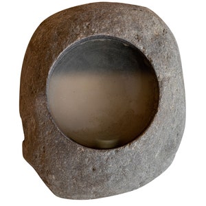 Op de afbeelding: Een grijze, ovale stenen kom met een cirkelvormige opening in het midden. De kom heeft een ruw, getextureerd oppervlak en een glad interieur. De opening onthult een gaasscherm. De kom is ge&iuml;soleerd op een witte achtergrond.