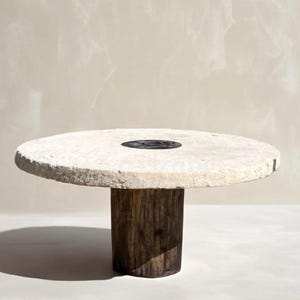 May include: A round, white stone table top with a black metal insert sits on a dark brown wooden pedestal.