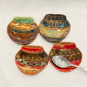 May include: Four ceramic spoon rests in a variety of brown, red, and green colors with geometric patterns. The spoon rests are shaped like small bowls.