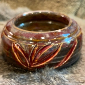 May include: A small, round, red and brown ceramic bowl with a leaf design. The bowl has a glossy finish and is perfect for holding small items.