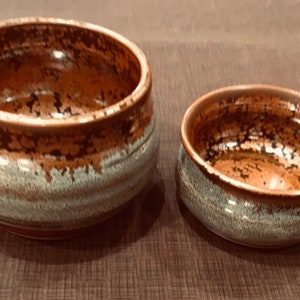 May include: Two ceramic bowls with a brown and white glaze. The larger bowl is wider and shallower than the smaller bowl.