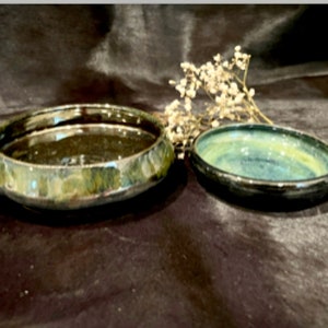 May include: Two ceramic bowls, one larger than the other, with a dark green and blue glaze. The larger bowl has a wider rim and a more rounded shape. The smaller bowl has a more traditional shape.