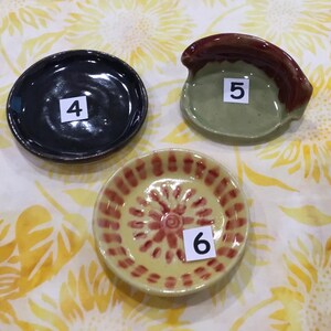 May include: Three ceramic dishes, one black, one green with a brown handle, and one yellow with red and brown designs. The dishes are numbered 4, 5, and 6.