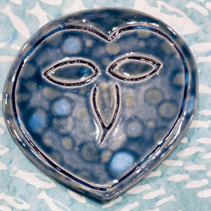 May include: A blue ceramic owl-shaped dish with a speckled glaze. The owl has a simple design with eyes, a beak, and a heart-shaped outline.