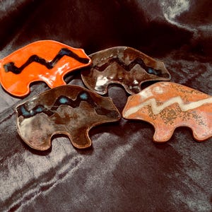 May include: Four ceramic bear-shaped dishes with different colored glazes and black, white, and blue zig-zag patterns.