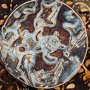 May include: A ceramic plate with a brown glaze and white designs of sea creatures. The plate features a turtle, a fish, and a crab.