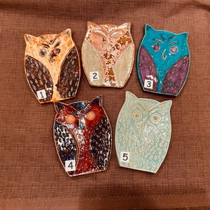 May include: Five ceramic owl-shaped dish soap holders. The owls are painted in different colors and patterns, including brown, blue, green, and pink. Each owl has a number painted on it, from 1 to 5.
