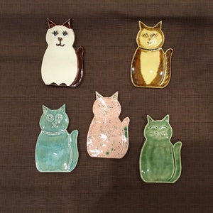 May include: Five ceramic cat dishware in various colors. The cats are in different poses, including sitting, standing, and lying down. The dishes are glazed in a variety of colors, including blue, green, pink, and brown.