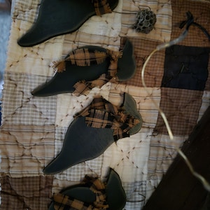 May include: Four dark green, flat, bird-shaped wooden ornaments, each adorned with a small, frayed, tan and black plaid fabric ribbon tied around the neck area. The ornaments are arranged in a vertical row, showcasing a smooth, matte finish.