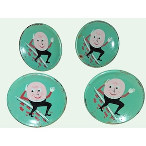 May include: A set of four round metal coasters featuring a light green background and a graphic illustration of a pink-faced character with a white collar and black clothing, depicted in a dynamic pose with visible signs of wear and oxidation.
