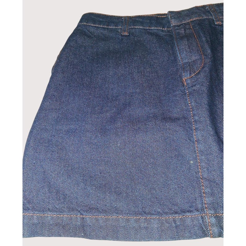 Pode incluir: Uma saia de ganga azul escura com costuras vis&iacute;veis em fio laranja-castanho contrastante. A saia tem um design cl&aacute;ssico de cinco bolsos e uma bainha reta. O tecido parece ser ganga de peso m&eacute;dio.