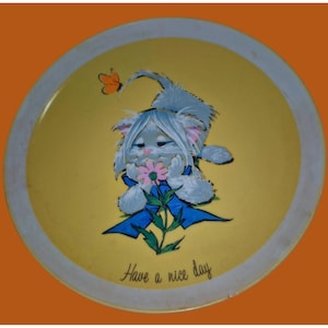 May include: A round, yellow tray with a white rim featuring a cartoon cat holding a flower. The cat is light blue with a blue bow and the text "Have a nice day". An orange butterfly is also present.