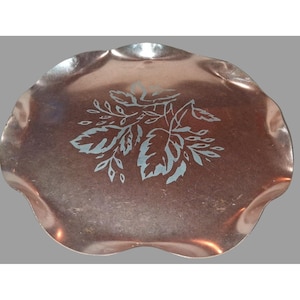 May include: A copper-toned, scalloped-edge tray with a floral design in light blue. The tray has a slightly irregular shape and a reflective surface. The floral design features leaves and stems. This decorative tray is suitable for serving or display.