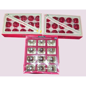 May include: Three boxes of Christmas ornaments. Two boxes contain red, shiny, faceted ornaments. The third box contains 12 shiny, silver glass ornaments. The boxes are red and white, with the text "VALUE PACK" on the red boxes.
