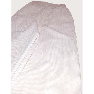 May include: Light pink waffle-weave pants with an elastic waistband. The pants have a relaxed fit and a textured surface. The fabric appears to be lightweight and suitable for casual wear. The pants have a simple, minimalist design.