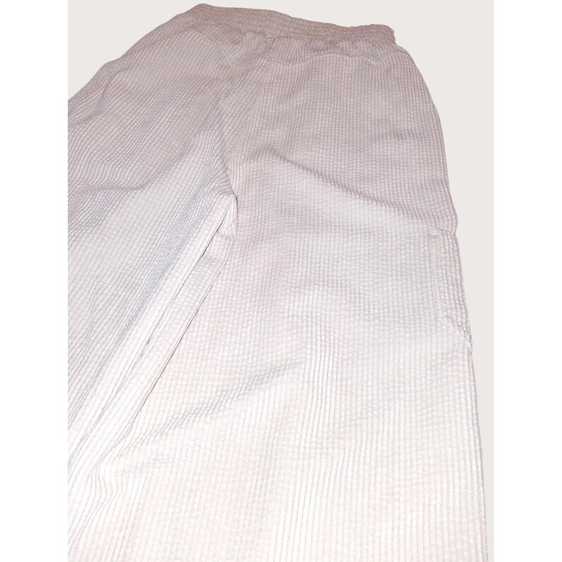 May include: Light pink waffle-weave pants with an elastic waistband. The pants have a relaxed fit and a textured surface. The fabric appears to be lightweight and suitable for casual wear. The pants have a simple, minimalist design.
