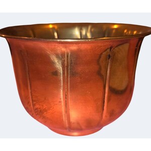 May include: A polished copper bowl with a rounded shape and vertical fluted detailing along the exterior surface. The bowl features a wide, smooth rim and a warm, metallic finish that reflects light across its curved, segmented body.