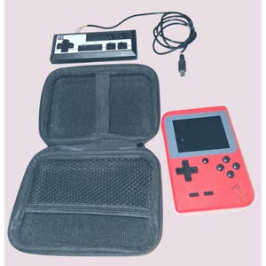 May include: A red handheld gaming console with a black screen and buttons, next to a black controller and a black carrying case. A black cable connects the controller. The case is open, revealing a mesh pocket.