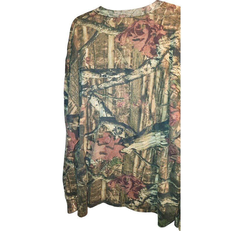May include: Long-sleeved camouflage shirt in shades of brown, green, and tan. The shirt features a crew neck and a pattern of branches and leaves, typical of hunting apparel.