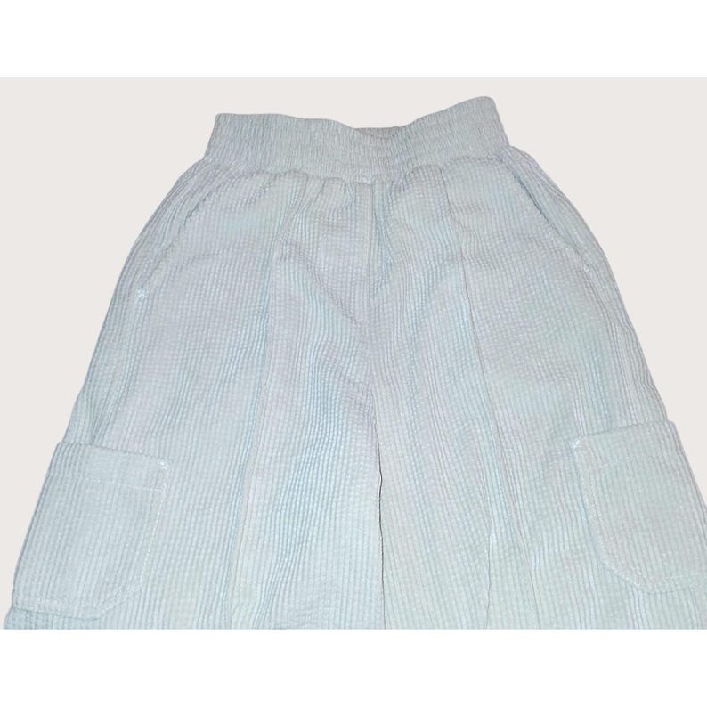 May include: Light blue corduroy pants with two front pockets. The pants have a high waist and a relaxed fit. The fabric has a ribbed texture. The pants are a solid color and appear to be made of a soft material.