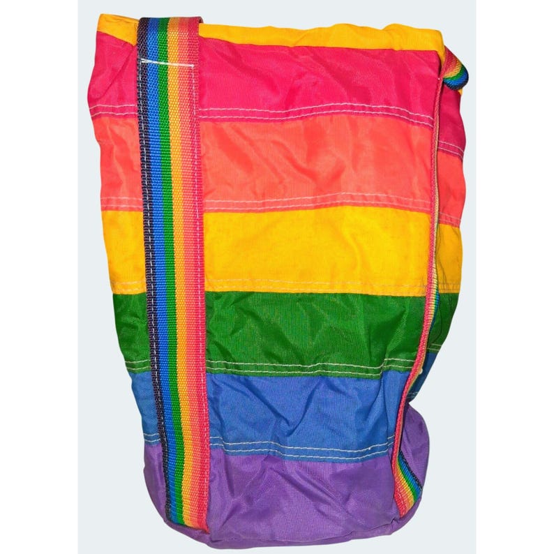 May include: A rainbow-striped tote bag with a matching rainbow strap. The bag features horizontal stripes in pink, orange, yellow, green, blue, and purple. The strap is a vertical rainbow pattern. The bag is made of a lightweight material.