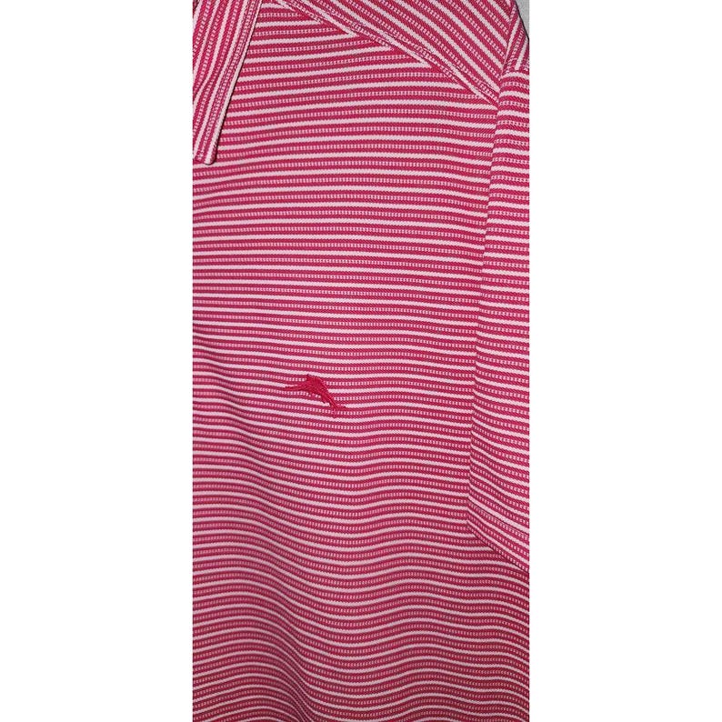 Puede incluir: Un polo a rayas rosas y blancas con cuello. La camisa presenta un peque&ntilde;o logotipo rojo en el pecho. La tela tiene un aspecto texturizado.