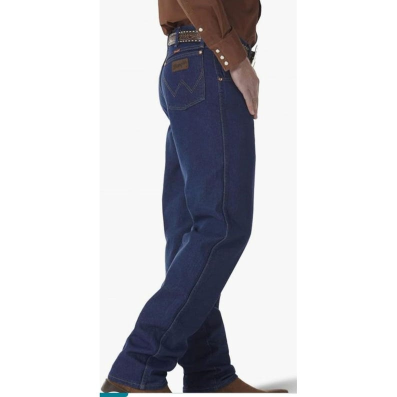 May include: Dark blue denim jeans with a classic five-pocket design. The jeans feature a straight leg cut and a Wrangler logo patch on the back pocket. The person is wearing a brown belt and a brown button-down shirt.