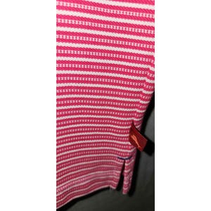 Puede incluir: Primer plano de un polo a rayas rosas y blancas. La camisa tiene un patr&oacute;n de punto texturizado y una peque&ntilde;a etiqueta roja con un logotipo. La camisa tiene un dobladillo inferior dividido.