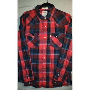 Puede incluir: Camisa a cuadros roja, negra y azul. La camisa de manga larga tiene dos bolsillos delanteros y botones blancos. La camisa de la marca Levi's está colgada en una percha negra.