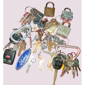 May include: A collection of keys and keychains, including a Ford keychain, a car key fob, and several padlocks. The keys are various shapes and sizes, with metal rings and clasps.