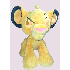 May include: A plush Simba toy from The Lion King. The toy is yellow with a pink nose, black-tipped ears, and embroidered facial features. The Simba plush is in a sitting position.