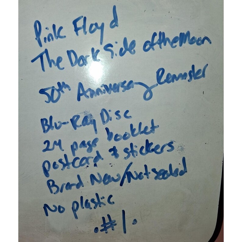 May include: A white dry-erase board with blue handwritten text that reads: Pink Floyd The Dark Side of the Moon 50th Anniversary Remaster, Blu-Ray Disc, 24 page booklet, postcard & stickers, Brand New/Not sealed, No plastic, #1.