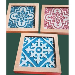Może przedstawiać: Trzy kwadratowe drewniane podkładki z dekoracyjnym wzorem płytek. Podkładki mają wzór niebieskiej i białej płytki, różowej i białej płytki oraz turkusowej i białej płytki.