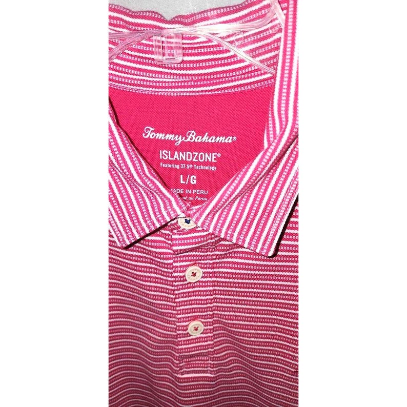 Puede incluir: Un polo a rayas rosas y blancas con el logo de Tommy Bahama Islandzone. La camisa tiene cuello y tres botones. La talla es L/G.