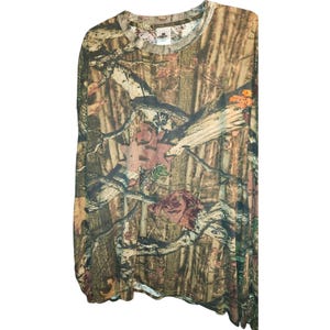 May include: Long-sleeved camouflage shirt with a crew neck. The shirt features a brown, green, and tan pattern with floral accents. The shirt has a tag on the neckline with the brand name. The fabric appears to be lightweight.
