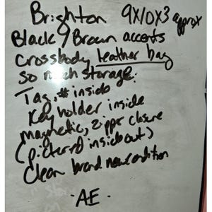 Puede incluir: Una pizarra blanca con texto escrito a mano en negro que describe un bolso bandolera de cuero Brighton con detalles en negro y marr&oacute;n, de aproximadamente 23x25x8 cm, con llavero, cierres magn&eacute;tico y de cremallera, y etiqueta interior.