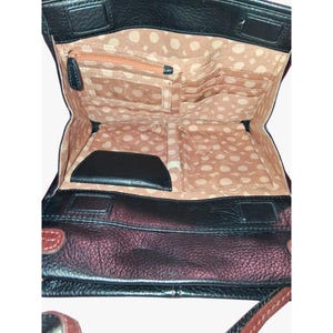 Puede incluir: Un bolso bandolera de cuero negro con cierre de solapa, que presenta un forro interior color canela con un patr&oacute;n de lunares blancos. El interior incluye un bolsillo con cremallera, una ventana transparente para identificaci&oacute;n y ranuras.