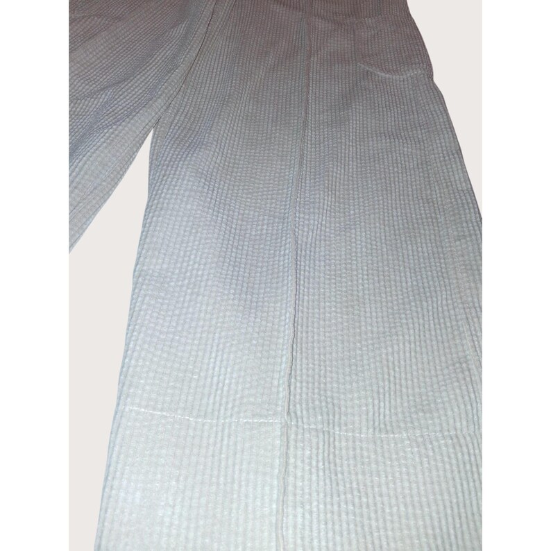 May include: Light blue, textured pants with a vertical ribbed pattern. The pants have a wide leg design and a seam down the front. The fabric appears to be a lightweight material, suitable for warmer weather.