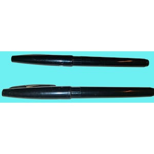 Może przedstawiać: Dwa czarne markery Sharpie są wyświetlane na jasnoniebieskim tle. Jeden marker ma założoną nasadkę, a drugi jest otwarty, odsłaniając końcówkę. Markery są cylindryczne z lekko zwężonym końcem.